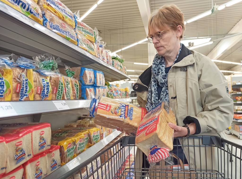 Frau vergleicht zwei Packungen Toastbrot im Supermarkt.