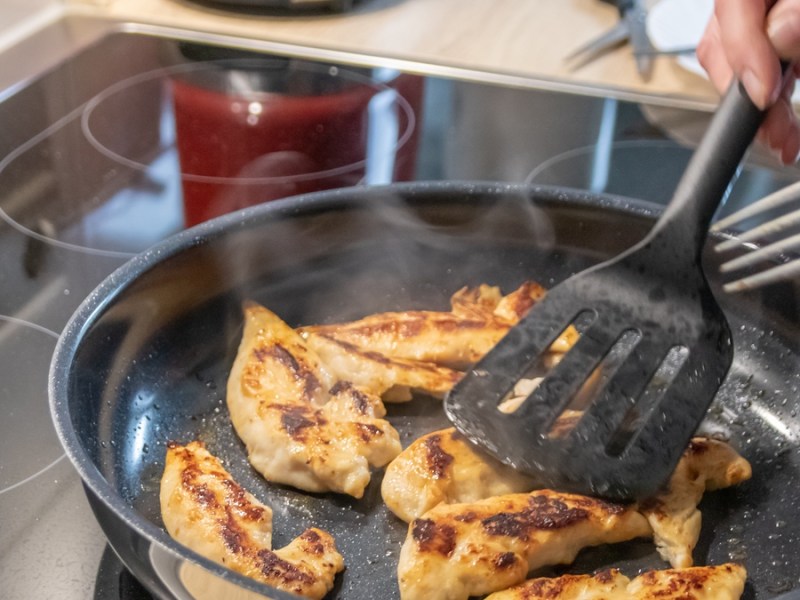 Hähnchen anbraten mit schwarzem Pfannenwender.