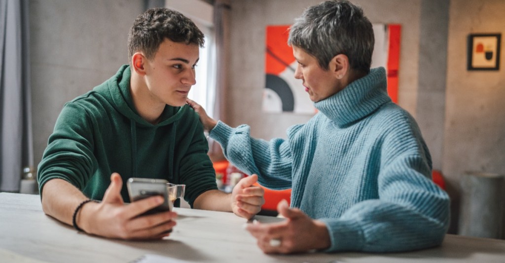 Teenager spricht mit seiner Mutter und hält dabei ein Handy in der Hand