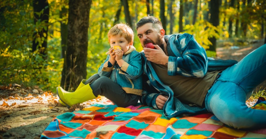 Vater und Sohn sitzen auf einer Decke im Wald und essen einen Apfel