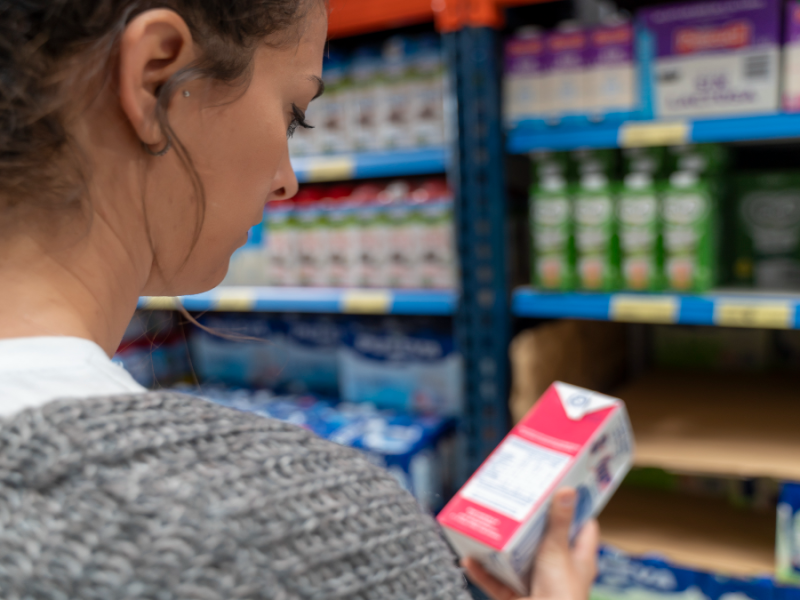 Frau schaut auf eine Tüte Milch im Supermarkt.