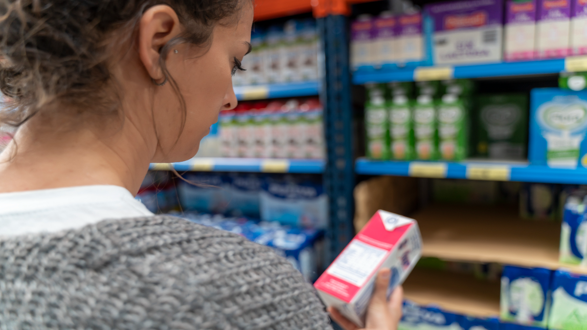 Frau schaut auf eine TÃ¼te Milch im Supermarkt.