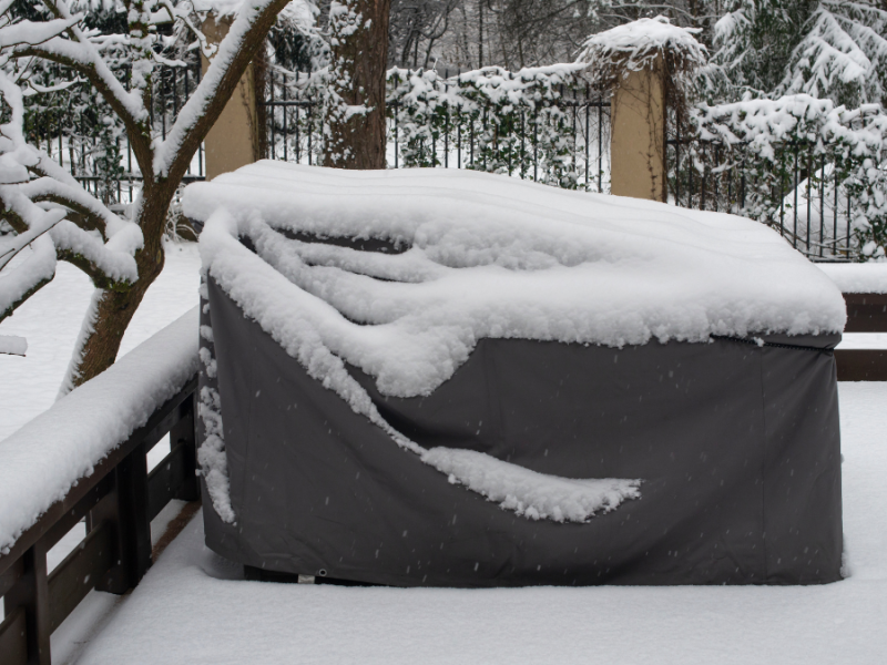 Mit einer Schutzfolie abgedeckte GartenmÃ¶bel, auf denen Schnee liegt.