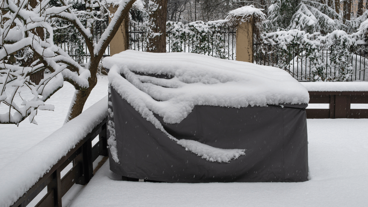 Mit einer Schutzfolie abgedeckte Gartenmöbel, auf denen Schnee liegt.