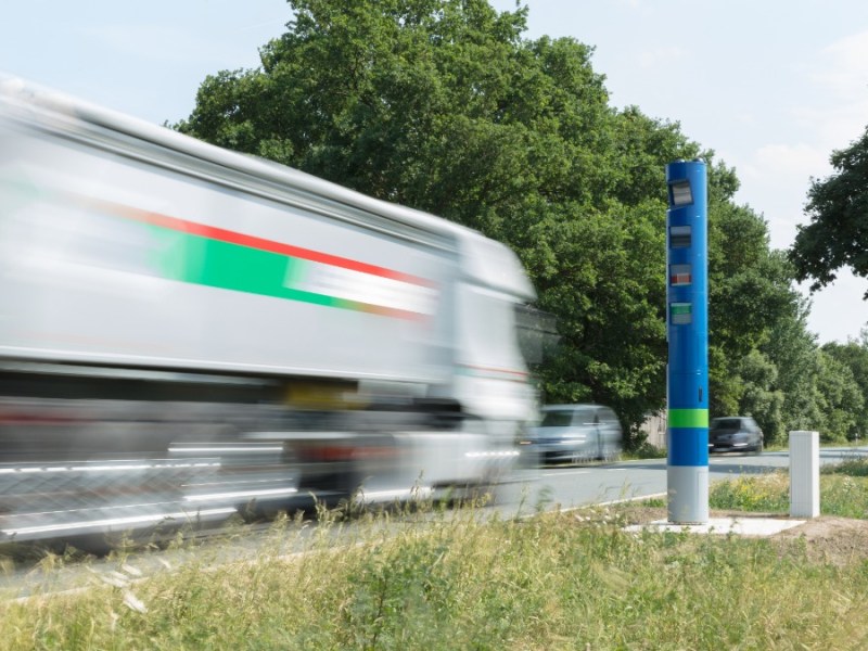 ein weißer Lkw fährt an einer blauen Säule am Straßenrand vorbei