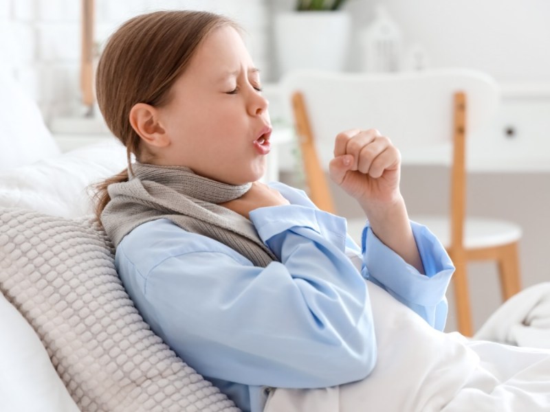 Mädchen liegt auf der Couch und hustet stark