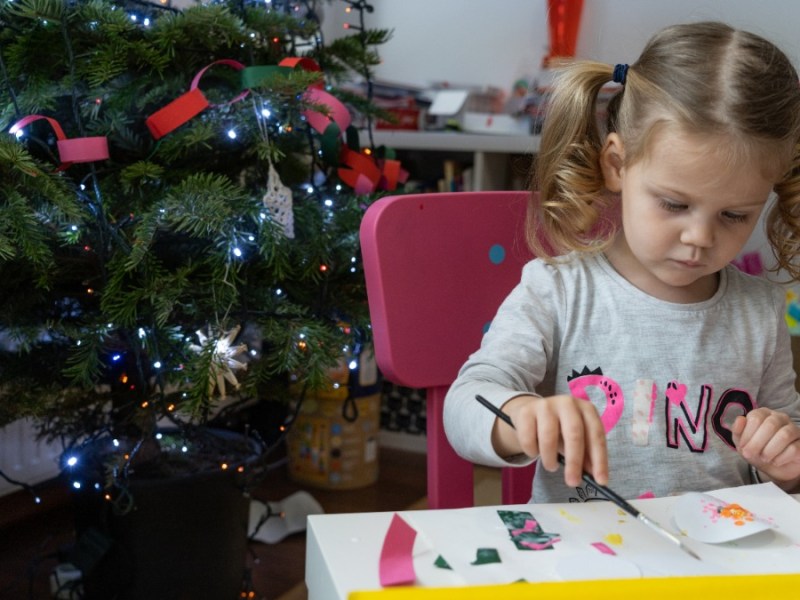 nÃ¼tzliche Geschenke Kinder: ein kleines MÃ¤dchen sitzt neben einem Weihnachtsbaum am Tisch und bastelt