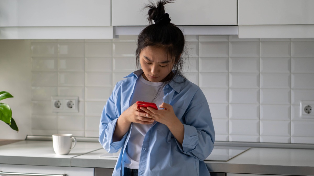 eine junge Frau steht in der Küche und tippt in ihr Telefon