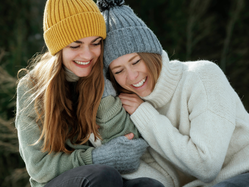 Zwei winterlich gekleidete Frauen lachen miteinander und umarmen sich