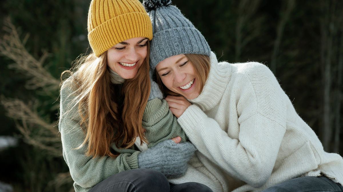 Zwei winterlich gekleidete Frauen lachen miteinander und umarmen sich