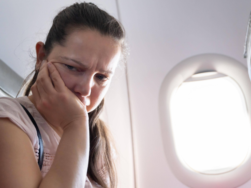 Frau mit Flugangst sitzt im Flugzeug und hat den Kopf auf die Hand gestÃ¼tzt.