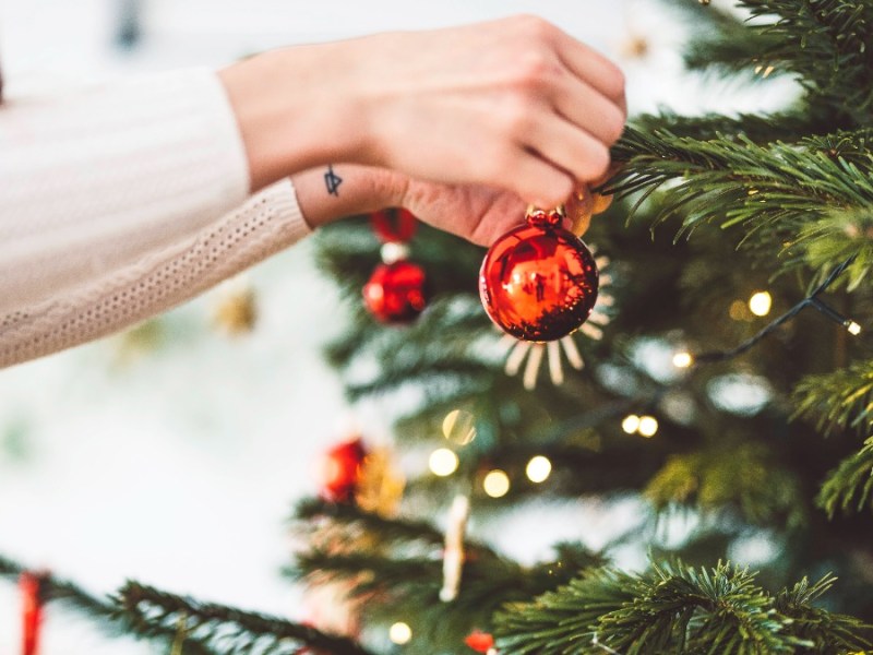 weihnachtlich dekorieren: eine Frau hängt eine Christbaumkugel an den Weihnachtsbaum