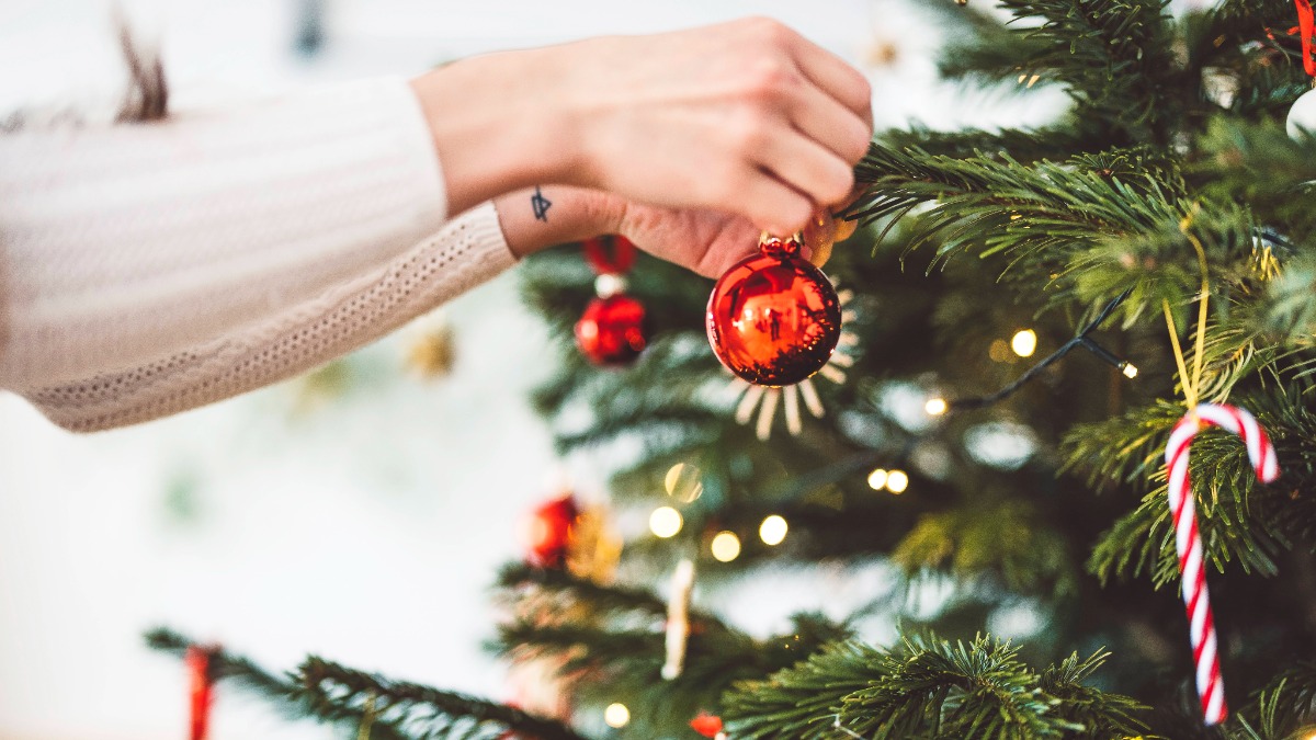 weihnachtlich dekorieren: eine Frau hÃ¤ngt eine Christbaumkugel an den Weihnachtsbaum