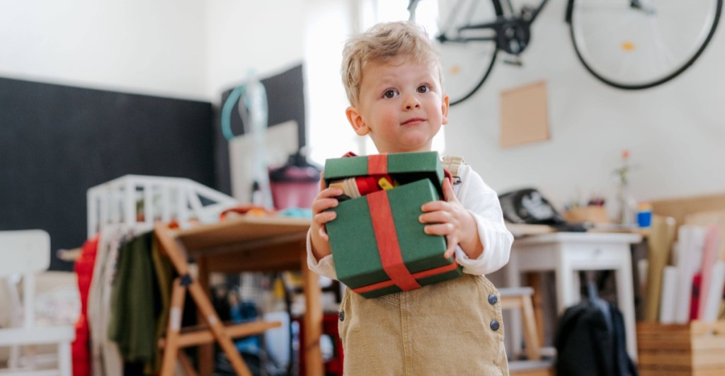 Geschenke für Kinder: kleiner Junge hält ein grünes Geschenk in der Hand