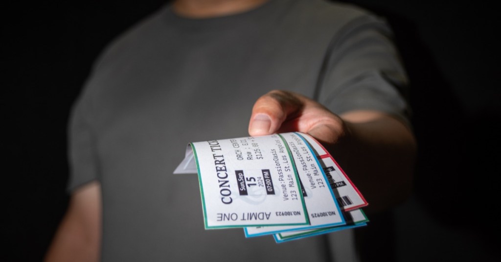 ein Mann hält drei Konzerttickets in der Hand