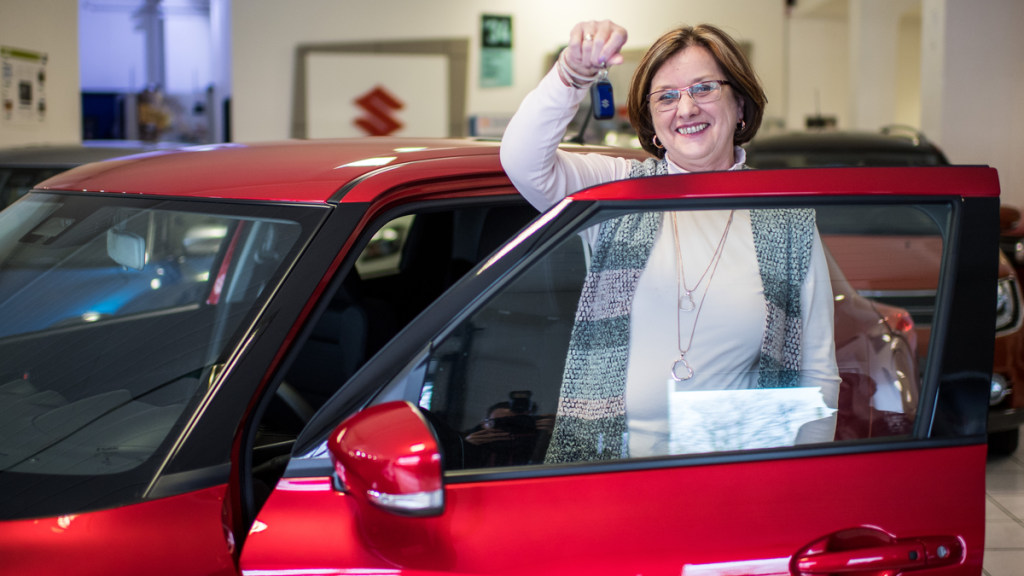 Frau posiert mit dem Autoschlüssel in der Hand vor einem roten Auto.