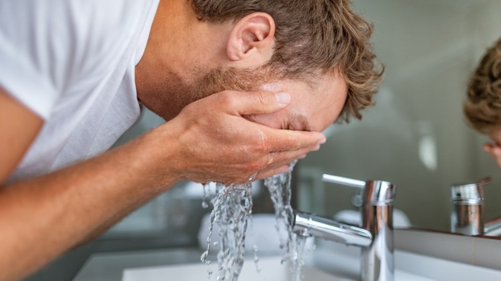 Ein Mann ist über das Waschbecken gebeugt und wäscht sein Gesicht.