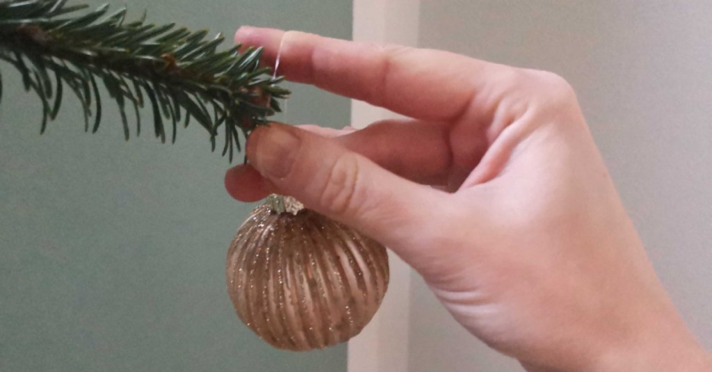 Eine Kugel wird mittels eines Gummibandes am Weihnachtsbaum befestigt