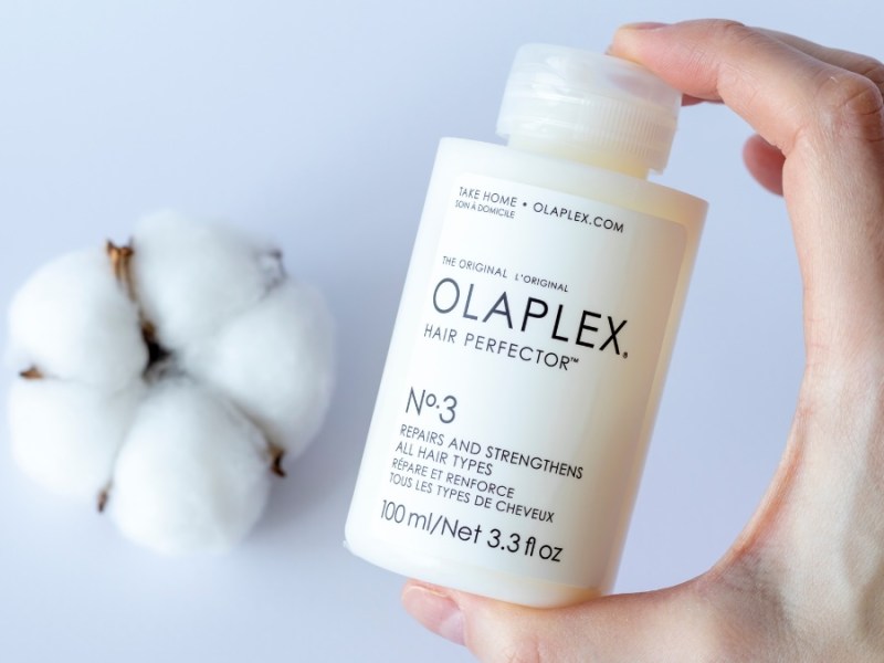 Eine Shampooflasche von Olaplex wird in die Kamera gehalten. Im Hintergrund liegt ein BaumwollbÃ¼schel.