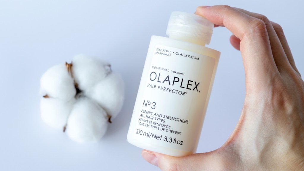 Eine Shampooflasche von Olaplex wird in die Kamera gehalten. Im Hintergrund liegt ein Baumwollbüschel.