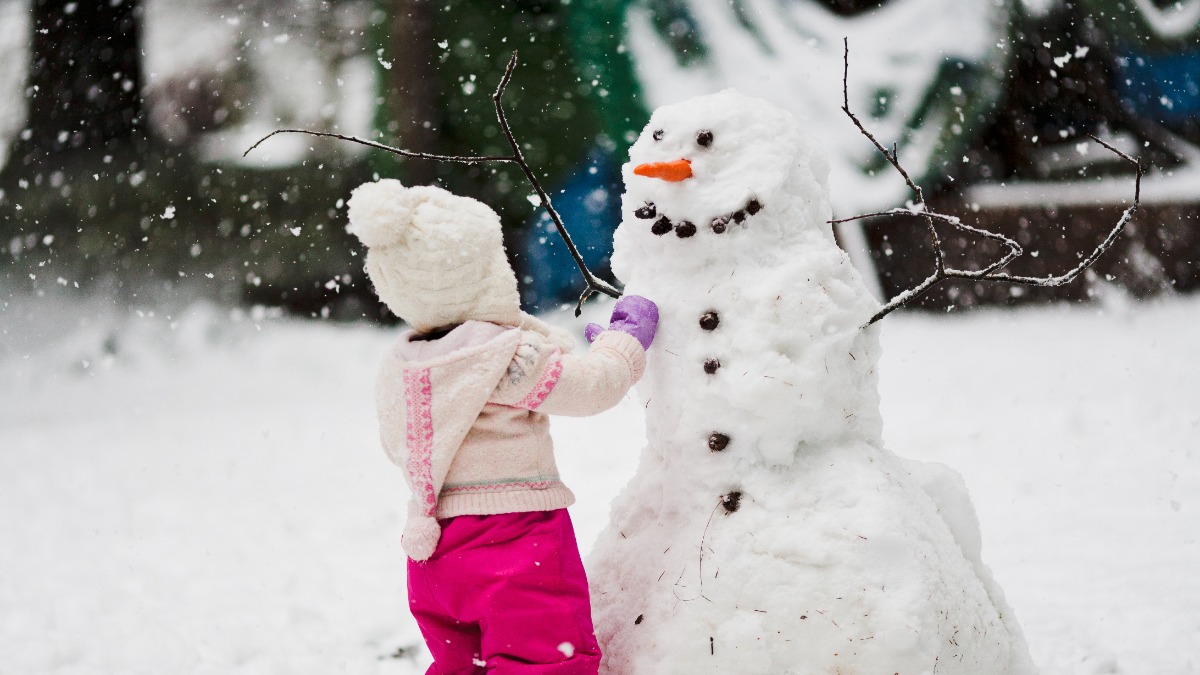 Schneemann bauen: ein kleines MÃ¤dchen steht vor einem Schneemann