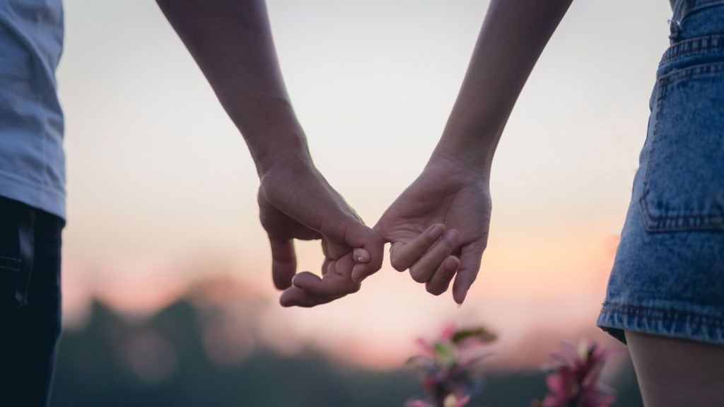 Ein Pärchen fässt sich an den kleinen Fingern an – im Hintergrund sieht man den Sonnenuntergang.