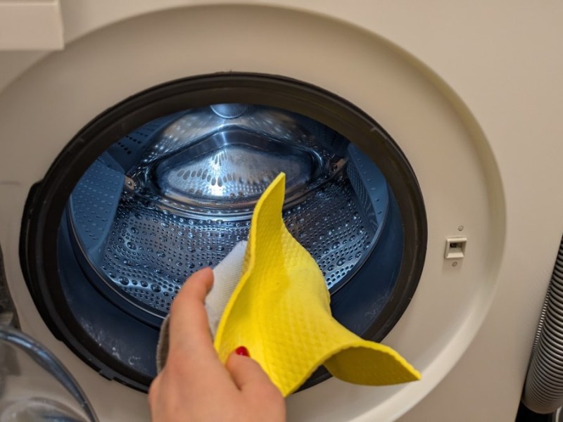 Eine Person steckt einen gelben Putzlappen in die WÃ¤schetrommel einer Waschmaschine.