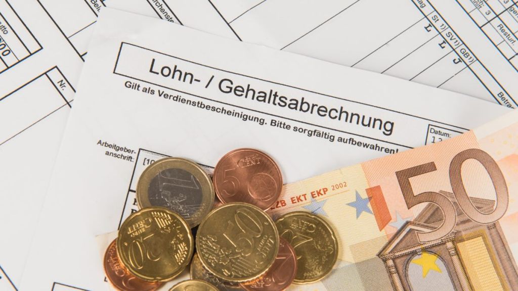 Eine Lohnabrechnung auf Papier und Bargeld, das darauf liegt.