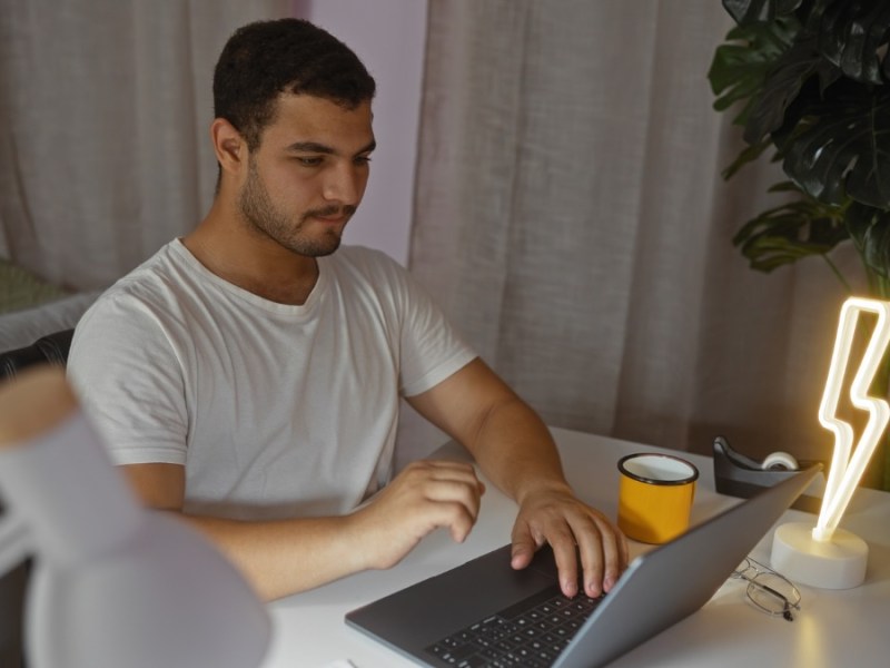 Ein Mann sitzt an einem Schreibtisch am Laptop.