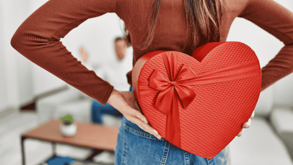 Valentintag Date-Box- Ideen, Frau hält rote Box in Herzform hinter ihrem Rücken versteckt