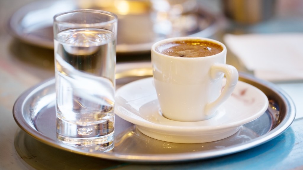 Ein silbernes Tablett mit einem Espresso und einem Glas Wasser stehen auf einem Tisch.