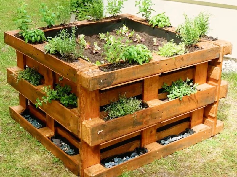 Ein Hochbeet, das aus Paletten gebaut wurde, steht in einem Garten.