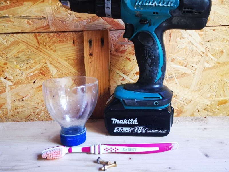 ein Akkuschrauber, eine Zahnbürste, zwei Schrauben und eine abgeschnittene Plastikflasche