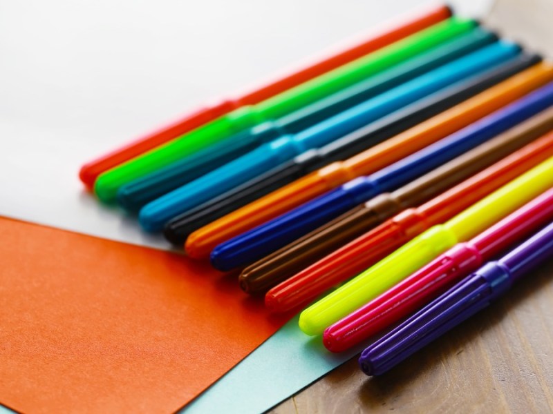 Verschiedene Filzstifte liegen neben farbigem Papier auf einem Tisch