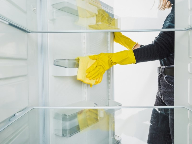 eine Frau wischt einen leeren Kühlschrank sauber