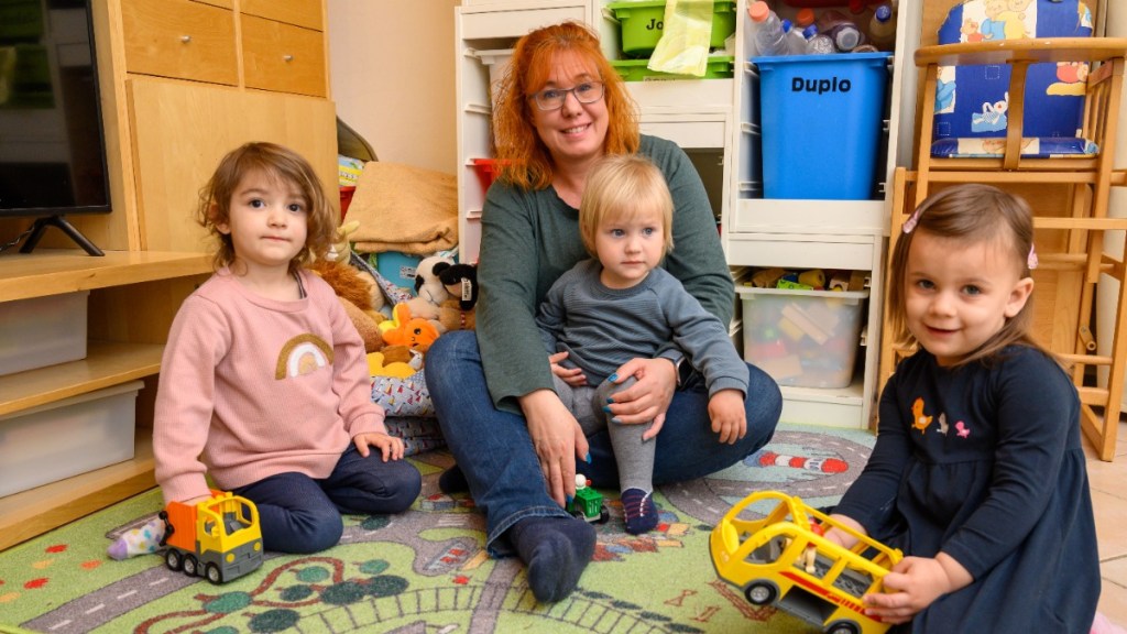 Eine Tagesmutter, die mit drei Kindern auf dem Boden sitzt.