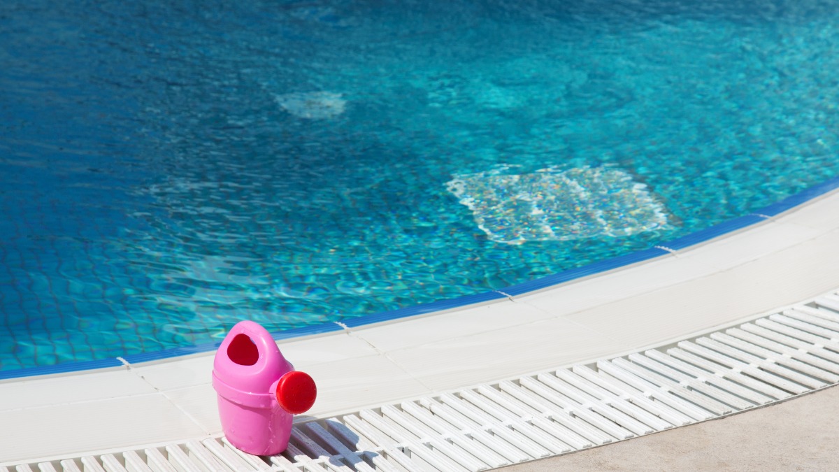 eine rosafarbene Kindergießkanne steht an einem Pool