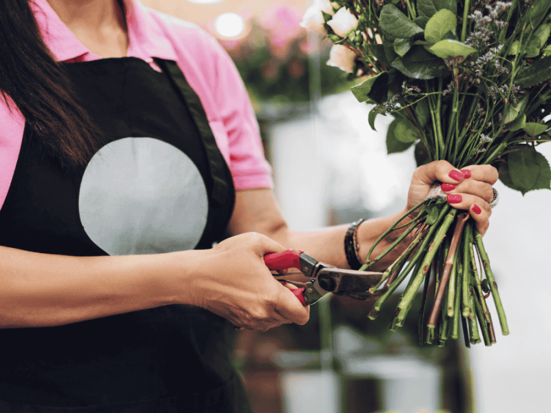 schnittblumen frisch halten, Frau mit Schürze schneidet Blumenstiele an